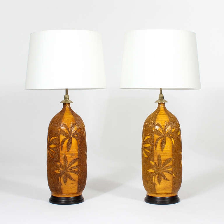 These are a great pair of etched palm tree pottery lamps, with alternating light and dark palm fronds heads on smooth and etched backgrounds. Fantastic ocher colors, on ebonized bases. These are extremely decorative lamps, with a great presence.