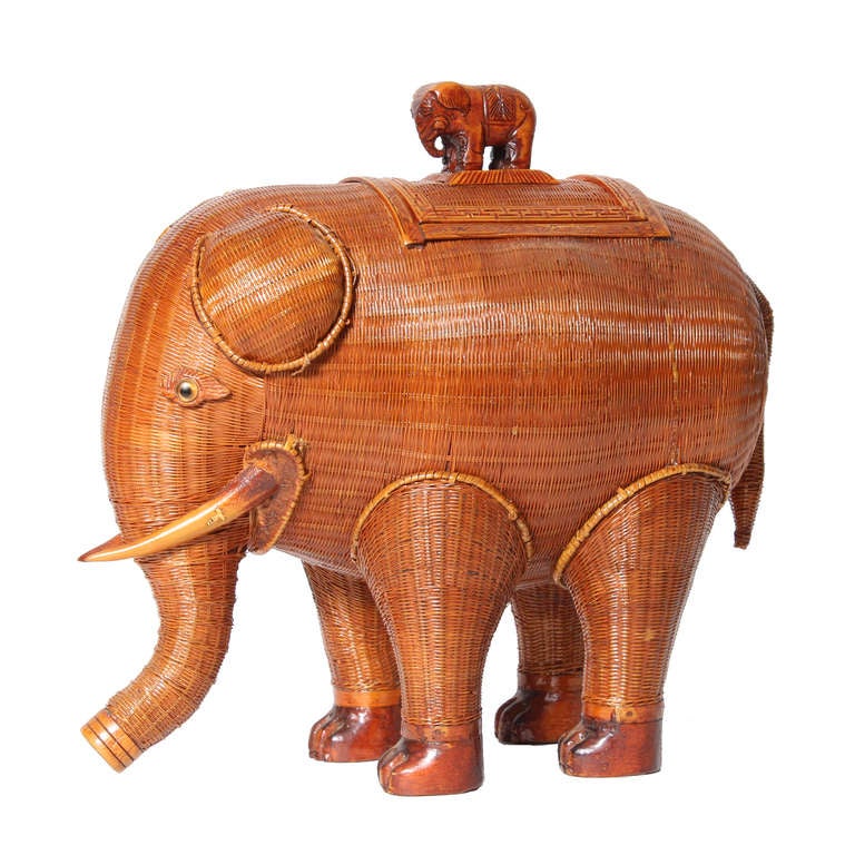 A very charming, extremely well woven wicker elephant box with glass eyes,wood feet, tusks, and baby elephant rider.