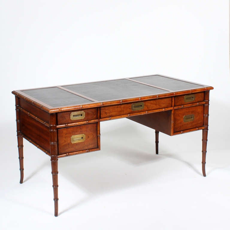 A faux bamboo mahogany knee hole desk with recessed campaign style pulls, a faux bamboo leg with ring turnings, and faux bamboo trimmed top and drawer dividers. A wonderful kick to the bottom of the leg, gives this desk a very sassy appeal. Tooled