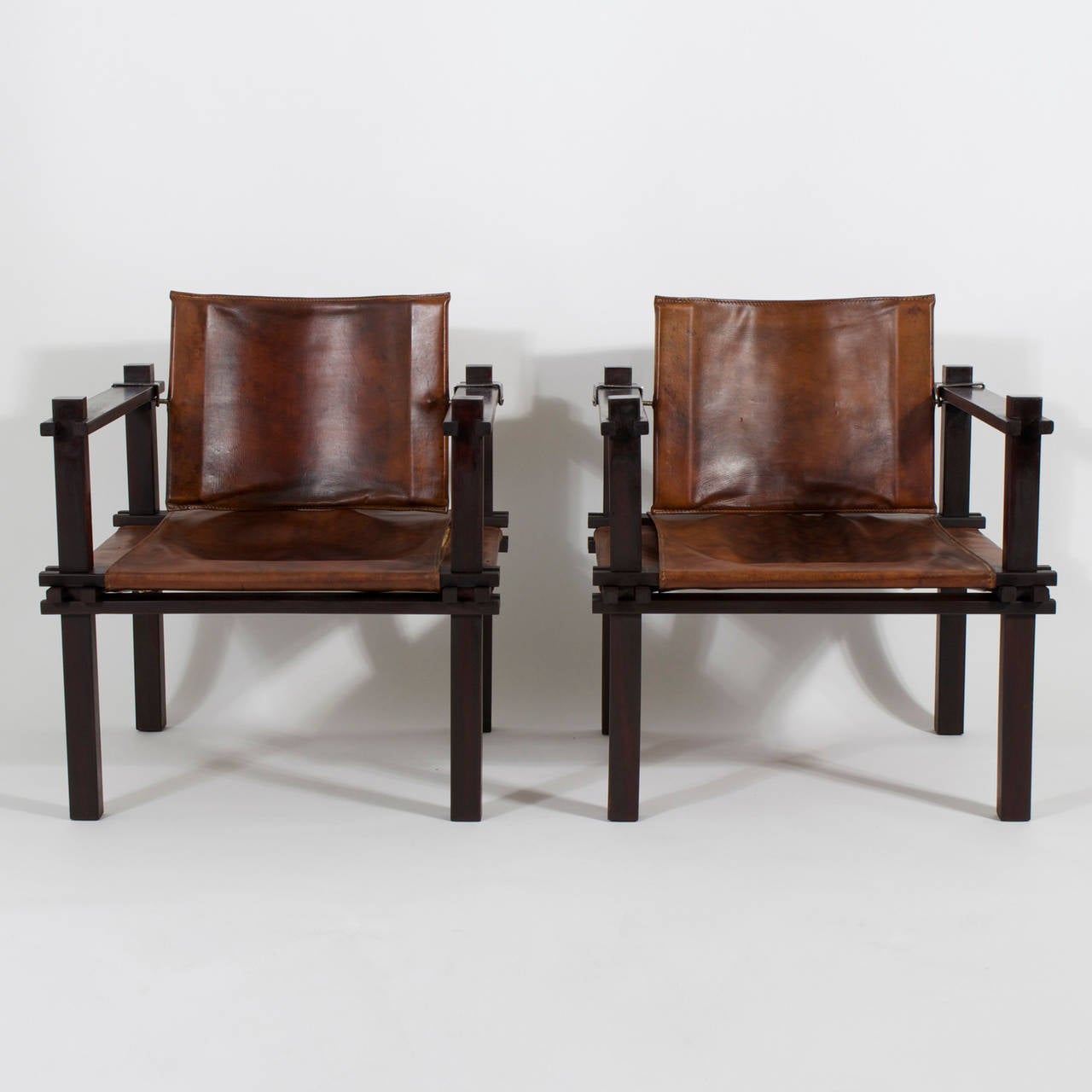 Rare pair of rosewood and perfectly aged leather Mid-Century Modern sling chairs with a rather important air about them. Possessing both an architectural structure and an inviting warmth, these Mid-Century chairs hit on several levels of the