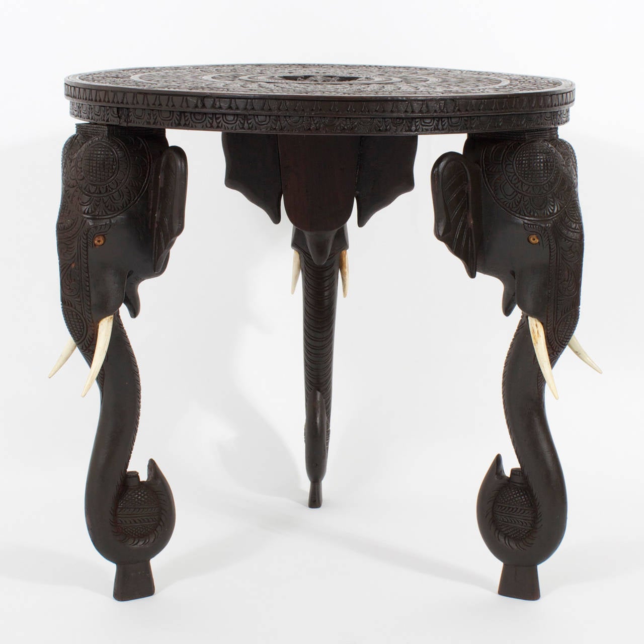 Exotic, vintage Anglo Indian occasional table, in a beautiful finish with 3 carved elephant head legs supporting a circular top carved in concentric rings of floral patterns and a figurative center.