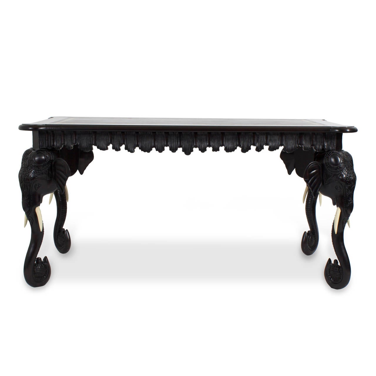 Exotic, vintage one drawer leather top writing table or desk featuring four carved wood elephant heads and trunks as legs, a carved and scalloped undulating pleated skirt, all in an ebonized finish with a tooled brown leather top. A tremendously
