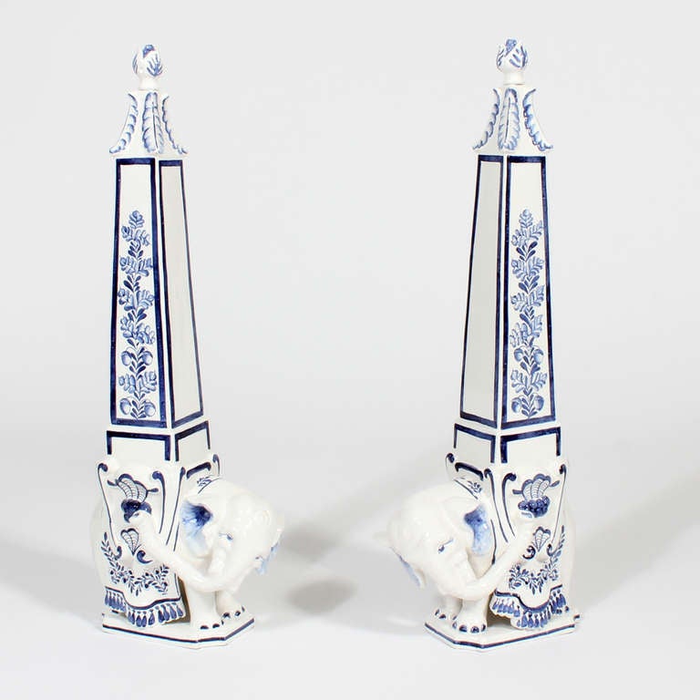 A pair of large blue and white porcelain elephant obelisks, with elephant figures supporting floral decorated tapering columns with removable stoppers. Made in Italy for Meiselman Imports.