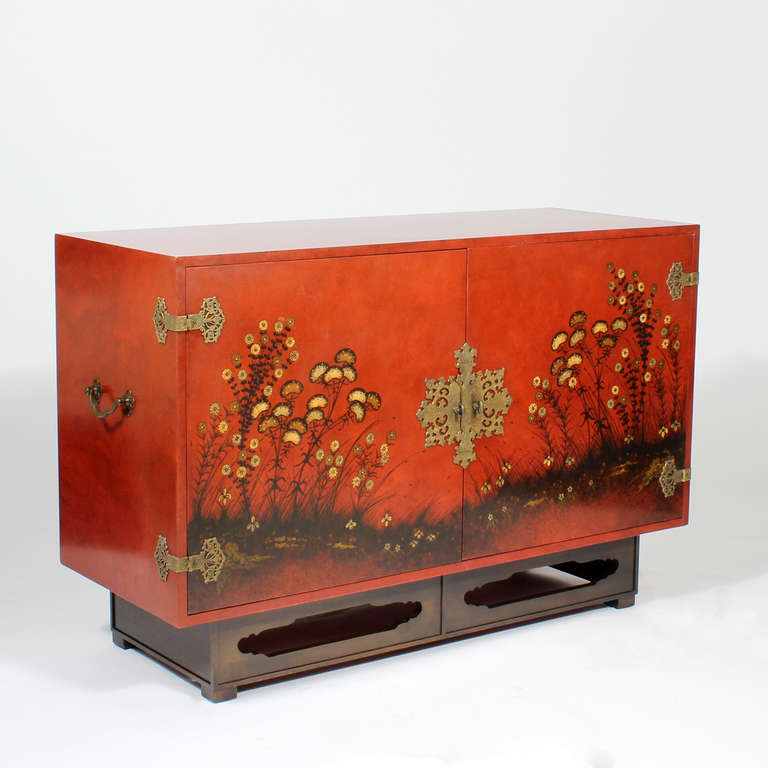 A modern version of a Chinoiserie design decorates this incredibly painted sideboard. Two large doors open to 2 pullout drawers and a long shelf. The case supported with a modified Chinese Chippendale style cut out base. Etched and pierced brass
