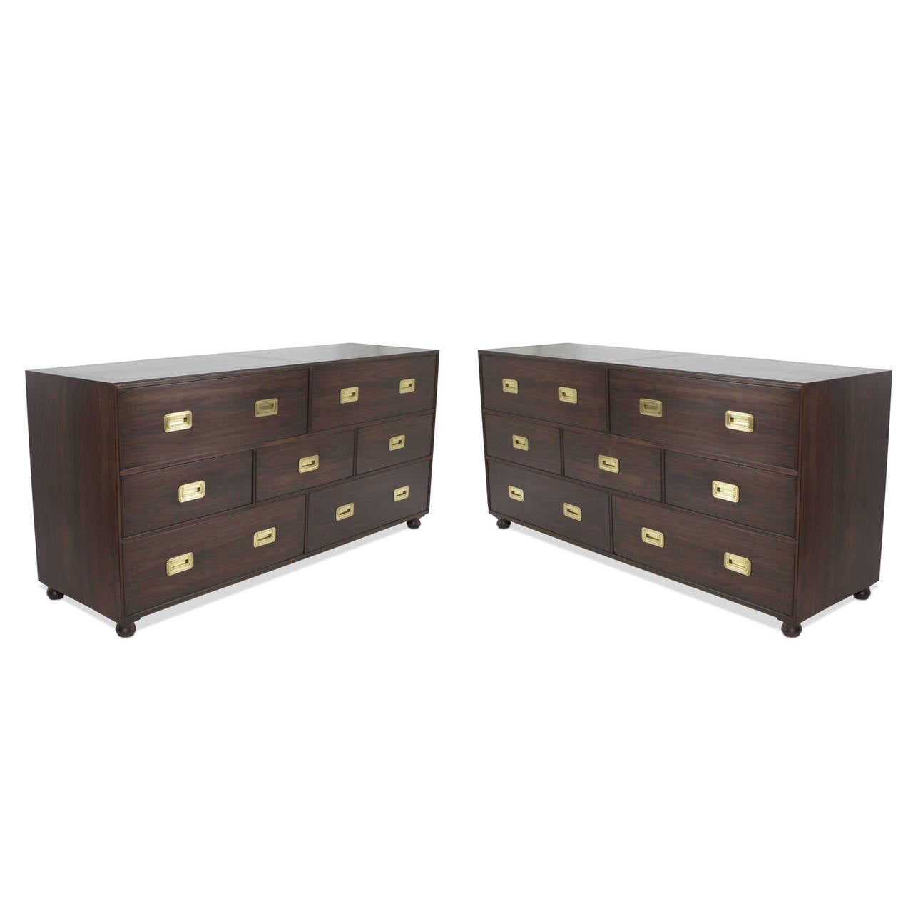 A pair of Baker Campaign style chests, dressers or sideboards, in a traditional form with a Mid-Century Modern vibe, all in a chic modern custom finish, complimented with brass inset hardware on seven off set drawers all-over bun feet. Newly
