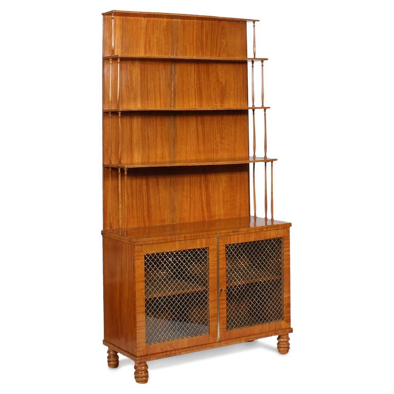 A bookcase or display shelves, in desirable satinwood, with gradated shelves, turned wood supports, brass wire with glass doors and a turned foot base. A very well made and elegant piece of furniture. Newly polished.