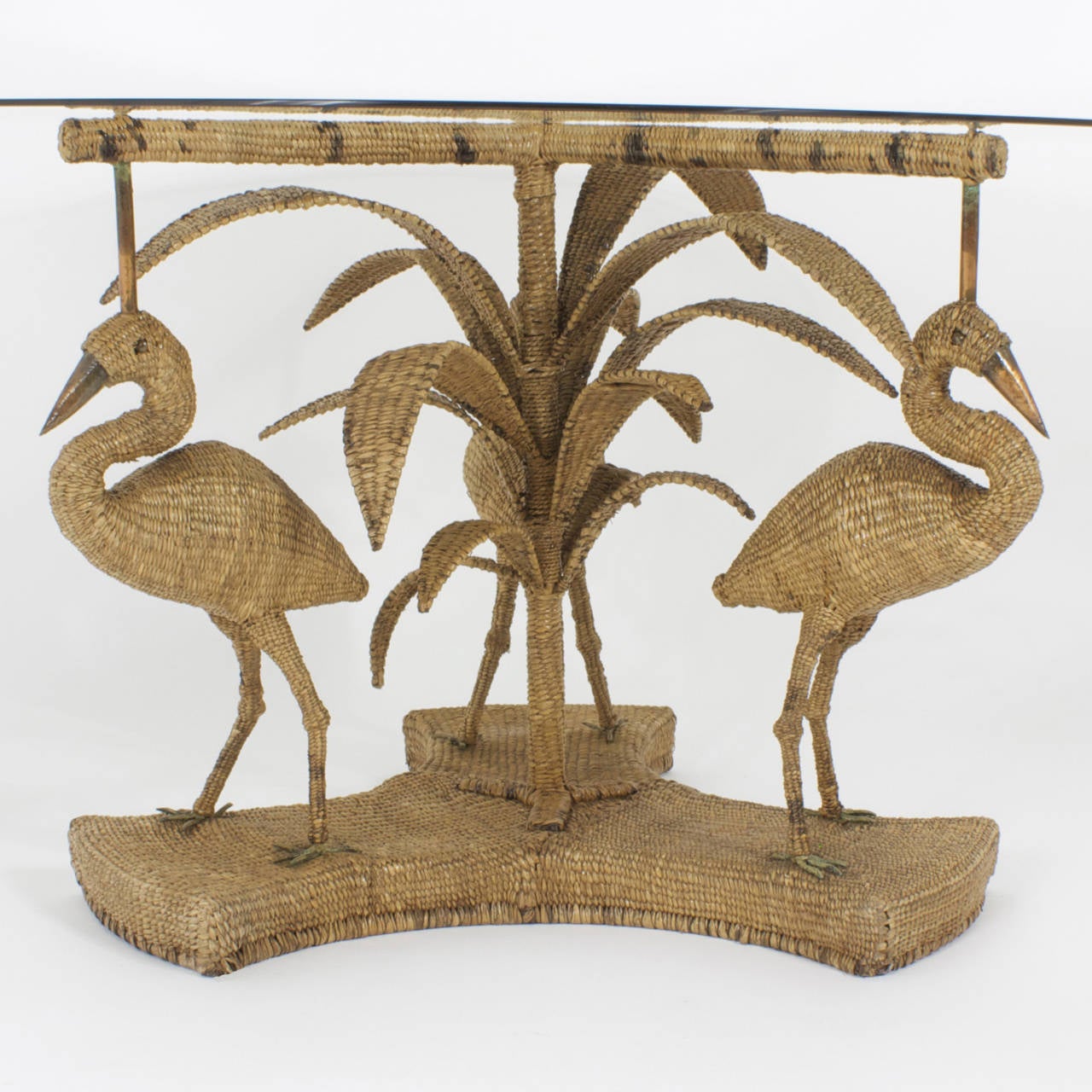 Whimsical, wicker or reed glass top dining table featuring a palm tree pedestal and large birds, possibly egrets or herons, with brass eyes, beaks and feet. The expertly woven rattan or reed, is tightly wound around a metal form. Folk Art, with
