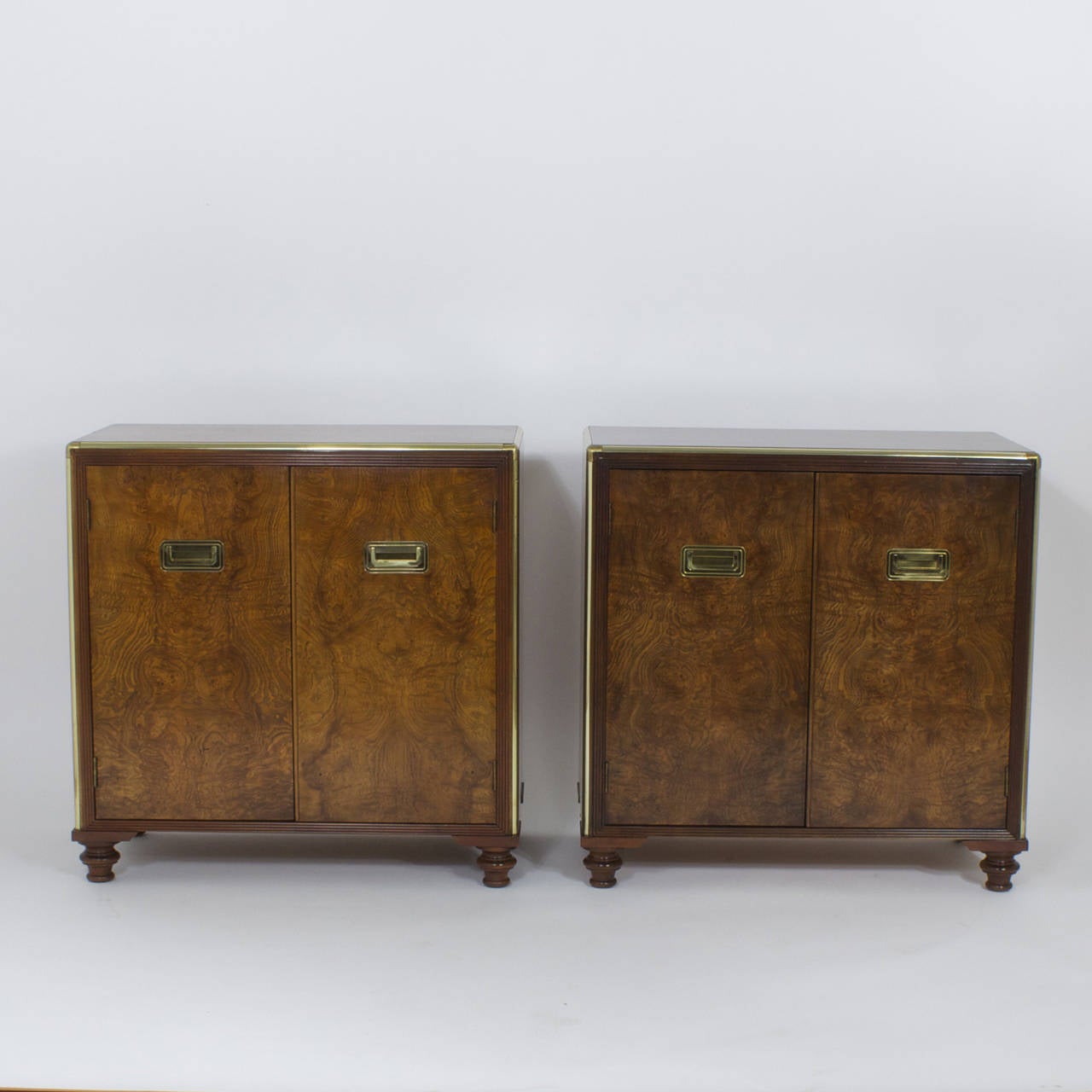 Pair of handsome, burled wood, cabinets, nightstands, chests or beside tables. Featuring campaign style brass hardware, turned feet and glass shelves behind 2 doors. Possibly by Baker. Perfect as bedside tables, or as end tables in the living room. 