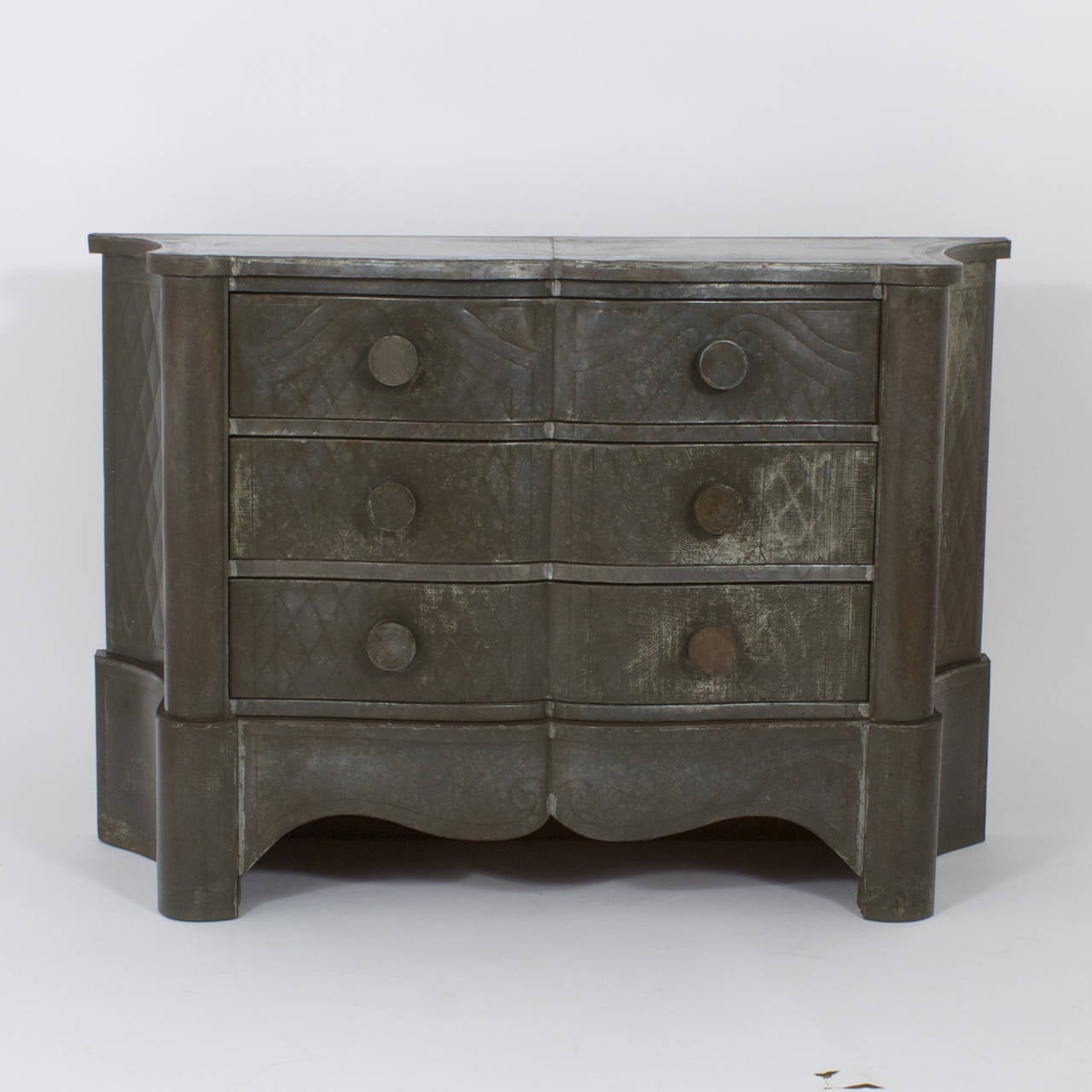 Rustic and rare early 20th century Mexican three-drawer chest entirely clad in tin with a charming oxidized patina, scalloped front and concave sides. This handsome piece features an embossed harlequin pattern on the front and sides with classic