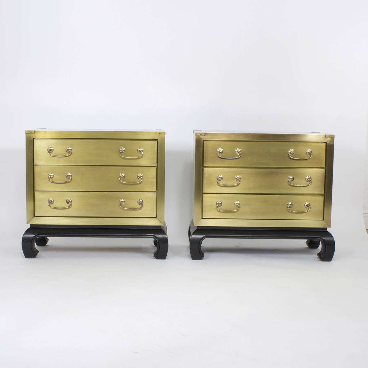 Chic pair of Mid-Century, Asian Modern style three-drawer brass nightstands with a warm glowing finish and elegant hardware, resting on ebonized bases, all perfectly proportioned and ready to shine as tables, chests or nightstands. These work well