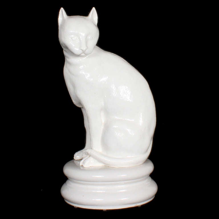 It is hard to tell what this seated cat figure is made of, perhaps a combination of terra cotta pottery and porcelain, the base appears to be porcelain, and the cat appears to be pottery.  Either way, the white lightly crazed glaze and the lightly