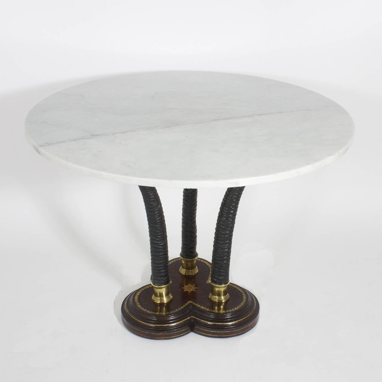 A very intriguing and handsome centre table signed Maitland-Smith. Featuring a white with marble top of strong grey veins that rests over three faux antelope horn legs with polished brass cuffs. The base is a clover shape with triple plinth