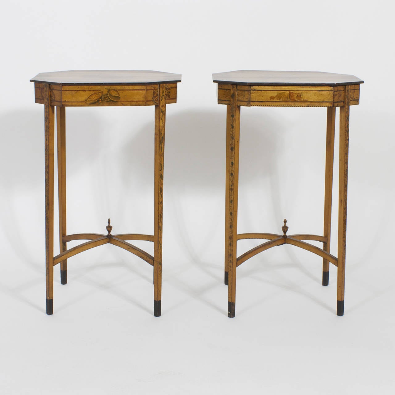 Elegant pair of satinwood tables or stands with hand-painted flowers and leaves on a semi hexagonal top. These tables feature sides decorated with nautical inspired seashell paintings between darker wood banding and a striped inlaid edge. Complete