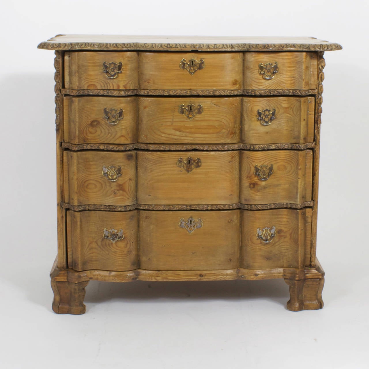 A rare 18th century French commode or dresser having a well-worn top with scalloped and carved edges. The four drawers are shaped to match the scalloped form of the top with floral carved dividers between each drawer. The whole chest is resting on