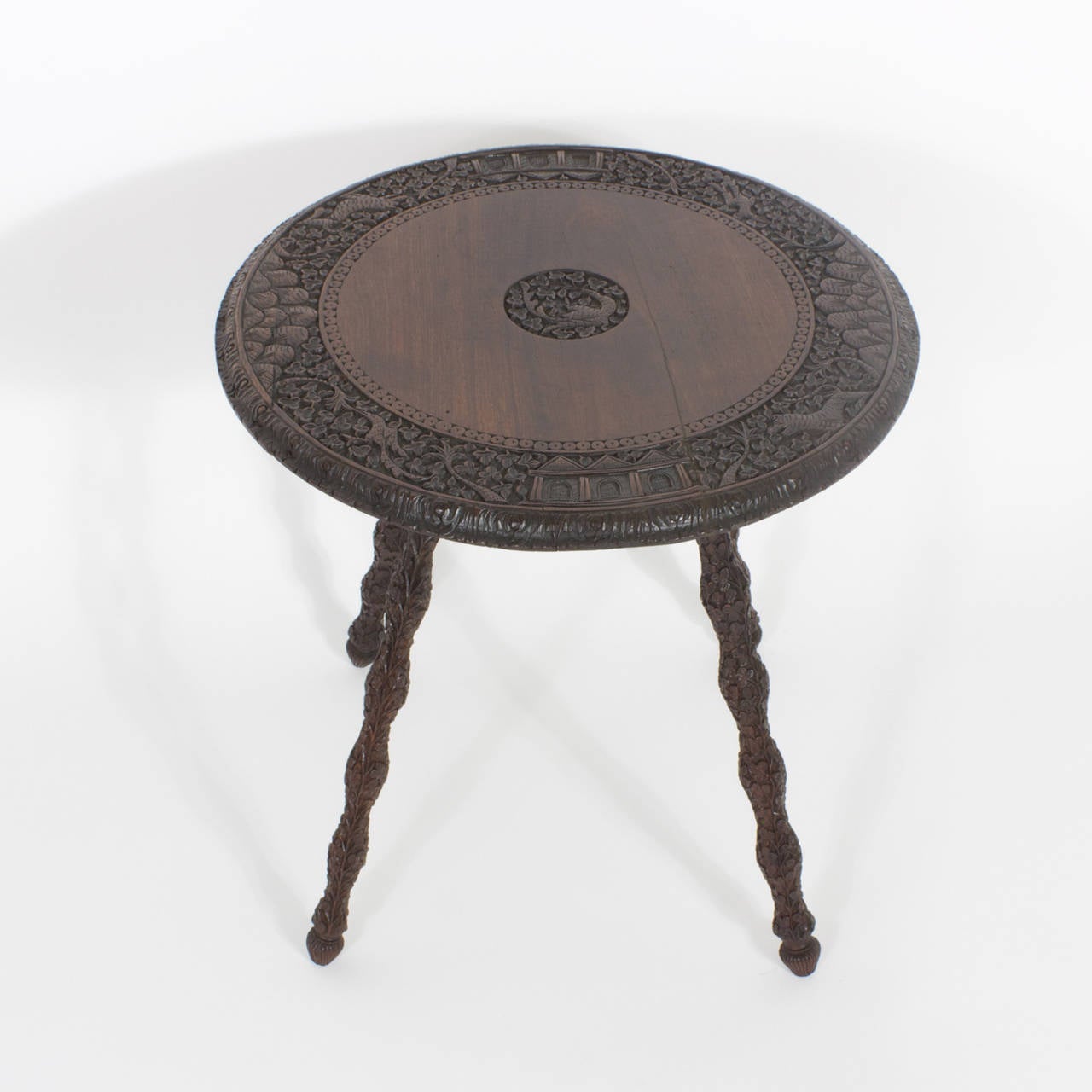 Rosewood Anglo Indian table with a round top. The top is intricately carved with a border of several motifs, including a jungle complete with big cat and mountains with architecture, as well as a center carving of a bird and flowers. Four legs