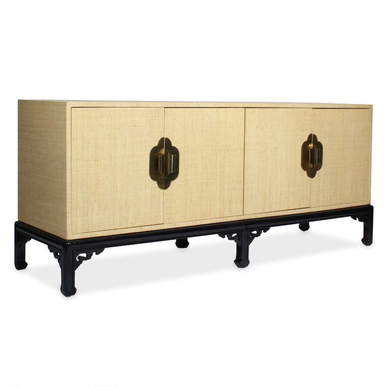 A modern vintage grasscloth wrapped sideboard or credenza in the manner of James Mont, with four doors, Asian inspired brass hardware and ebonized bracket base, in the Chinese Chippendale style. Very practical interior, with shelves and pullout