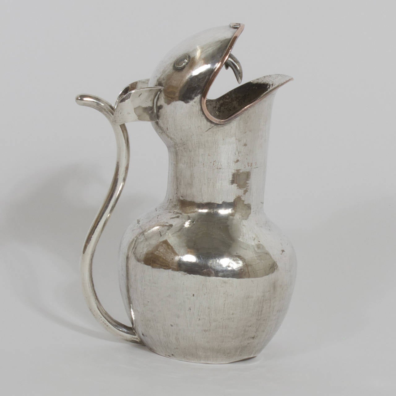 A whimsical Mid Century cat water pitcher. Silver plated and hand made. Baring an impressive pair of fangs and featuring copper lips and nose. A long graceful tail is used as a handle. Over all having a worm aged glow. Stamped on the bottom Chato