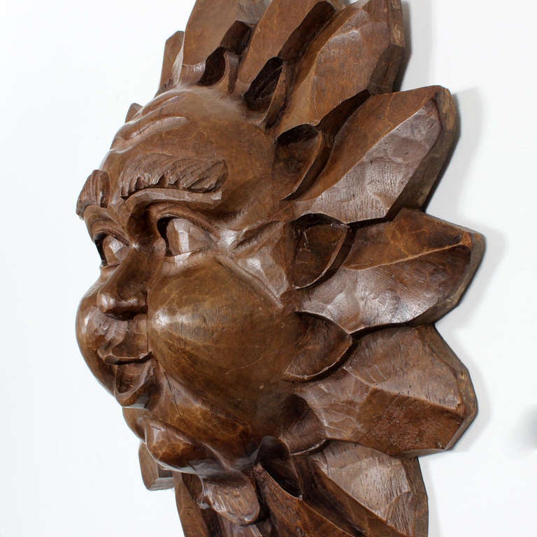 A large carved wood sun face, with deeply carved radiating rays and very robust facial features.

