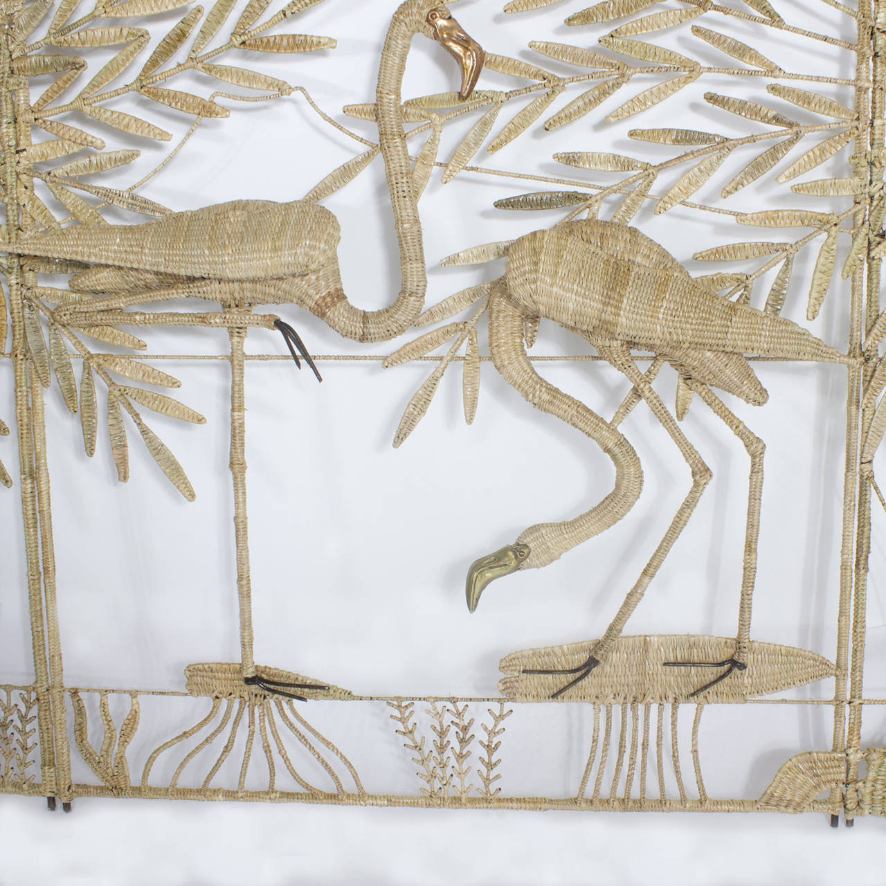 Sculptural Mario Torres three-panel screen constructed of a metal frame wrapped in wicker. Depicting a tropical scene with palm trees and flamingos sitting on lily pads and sea grass. The flamingos striking a familiar pose while one has a copper