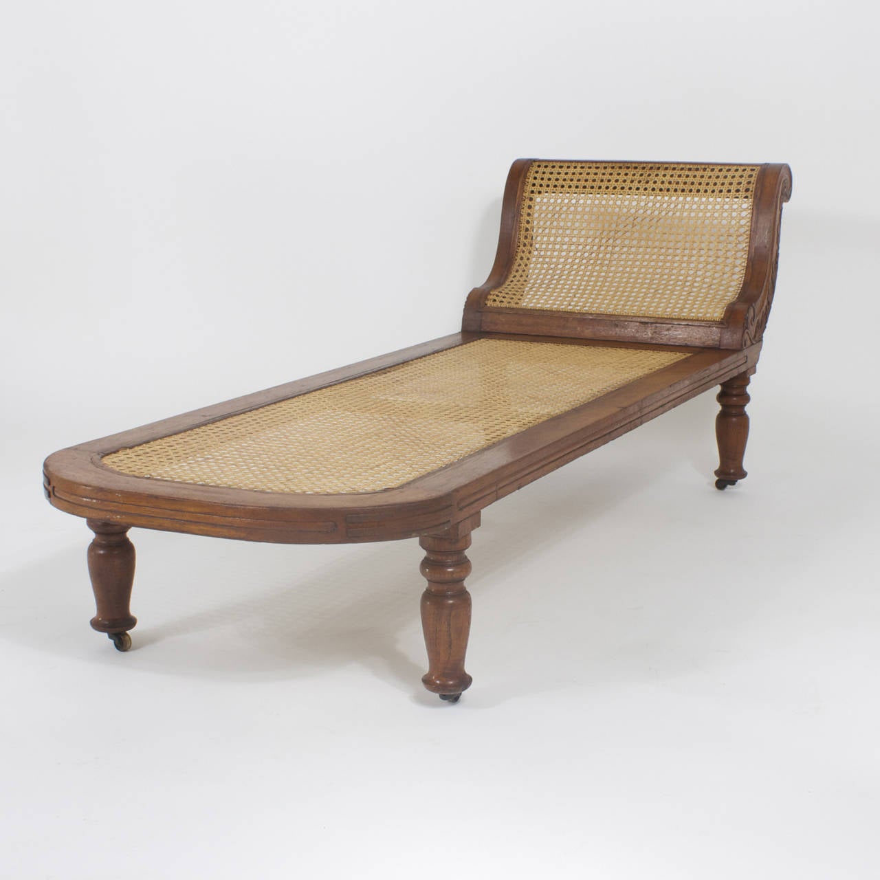 Antique West Indian chaise longue or recamier made from mahogany. Featuring caned seat and back, expertly carved back scrolling and turned legs with an unusual bell shape. Handmade construction and an over all elegant form. Another addition to our