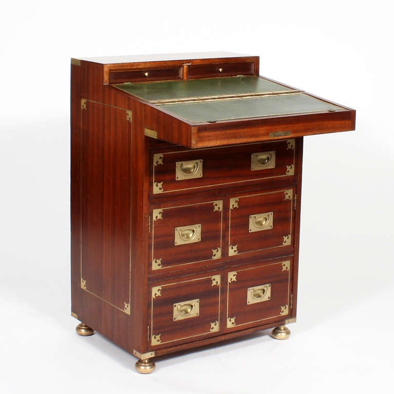 A lovely proportioned campaign chest, with a drop down top, containing a leather covered writing surface and 2 small drawers, in the interior. One false drawer, one operating drawer and 2 doors are the configuration of the exterior.  Brass inlaid