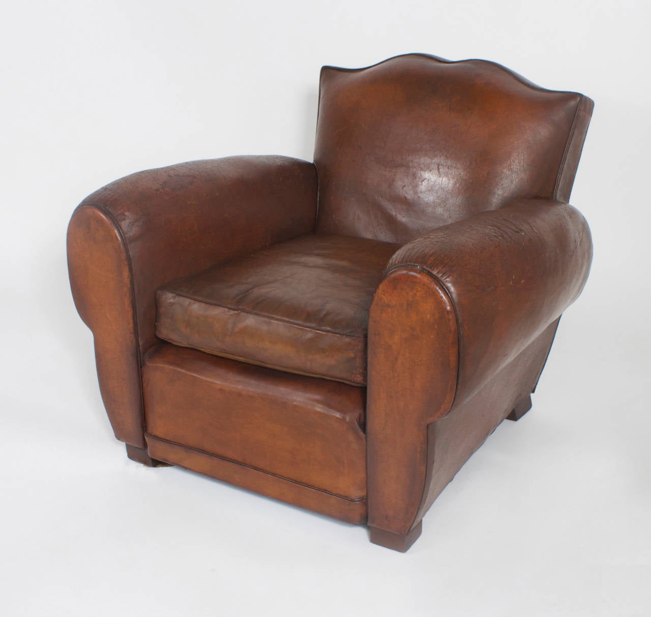 Classic pair of vintage French leather club chairs featuring scrolled tops, exaggerated bulbous arms, removable cushions and bun feet. Having just the right amount of wear, Art Deco streamline form and an inviting comfort. Hard to find them in this