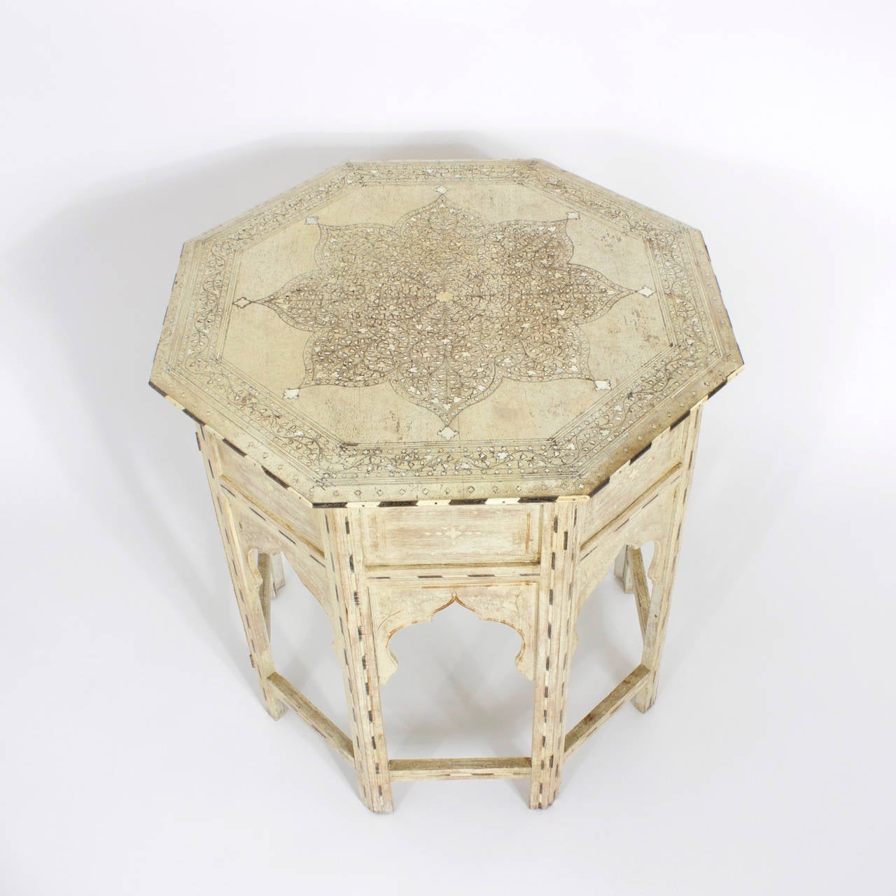 Moroccan octagon occasional table with interesting old worn paint that has acquired the look of old ivory. Having an intricately carved top with symbolic floral patterns and inlaid bone that is edged with alternating ebony and bone. The sides have