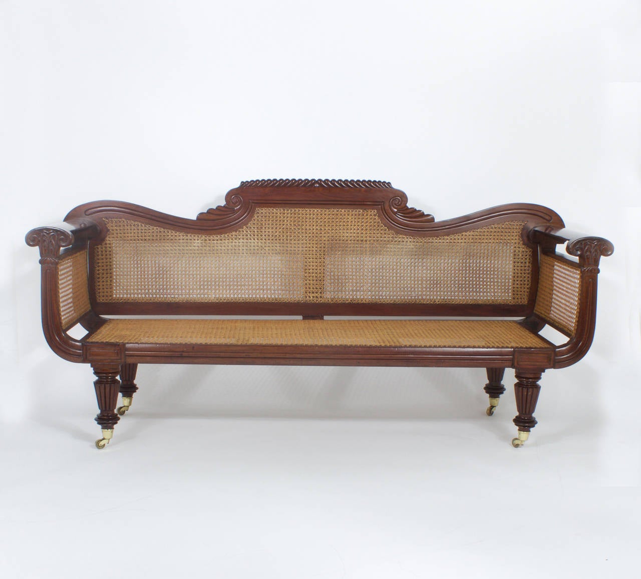Sophisticated West Indies caned mahogany sofa with elegant fluid lines and perfect proportions. Featuring breaking wave carvings on the back crest and floral design carving on the arm front. Sturdy turned and carved legs on brass casters.