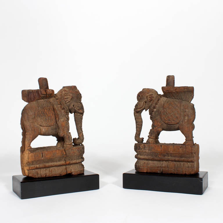 A pair of ancient, carved wood architectural remnants, depicting working elephants. Capturing the mystical essence of India, now presented on ebonized wood bases, carrying with them centuries of secrets.