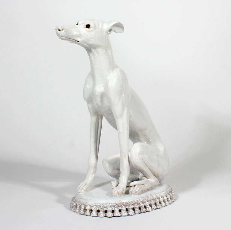 A large majolica or faience whippet or greyhound on a tasseled pillow, a thick white porcelain glaze over a terra cotta base.<br />
Very classic, with great body language and an expressive face.<br />
<br />
