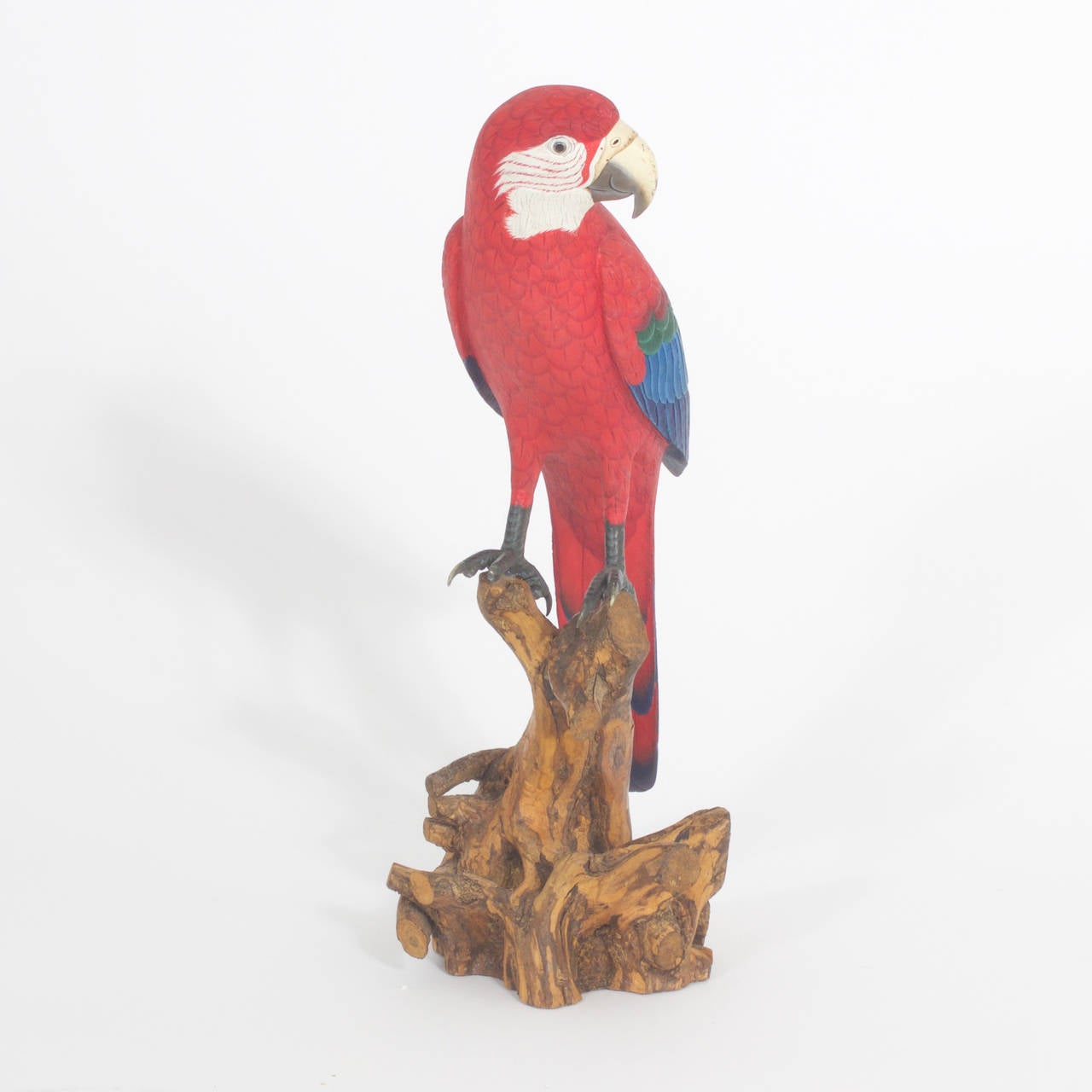 Carved and painted red parrot. Amazingly realistic wood carving of a multicolored Macaw parrot with glass eyes. Expertly carved and painted in hues of red, blue, green and white with real bird talons attached to the feet and presented on a tree