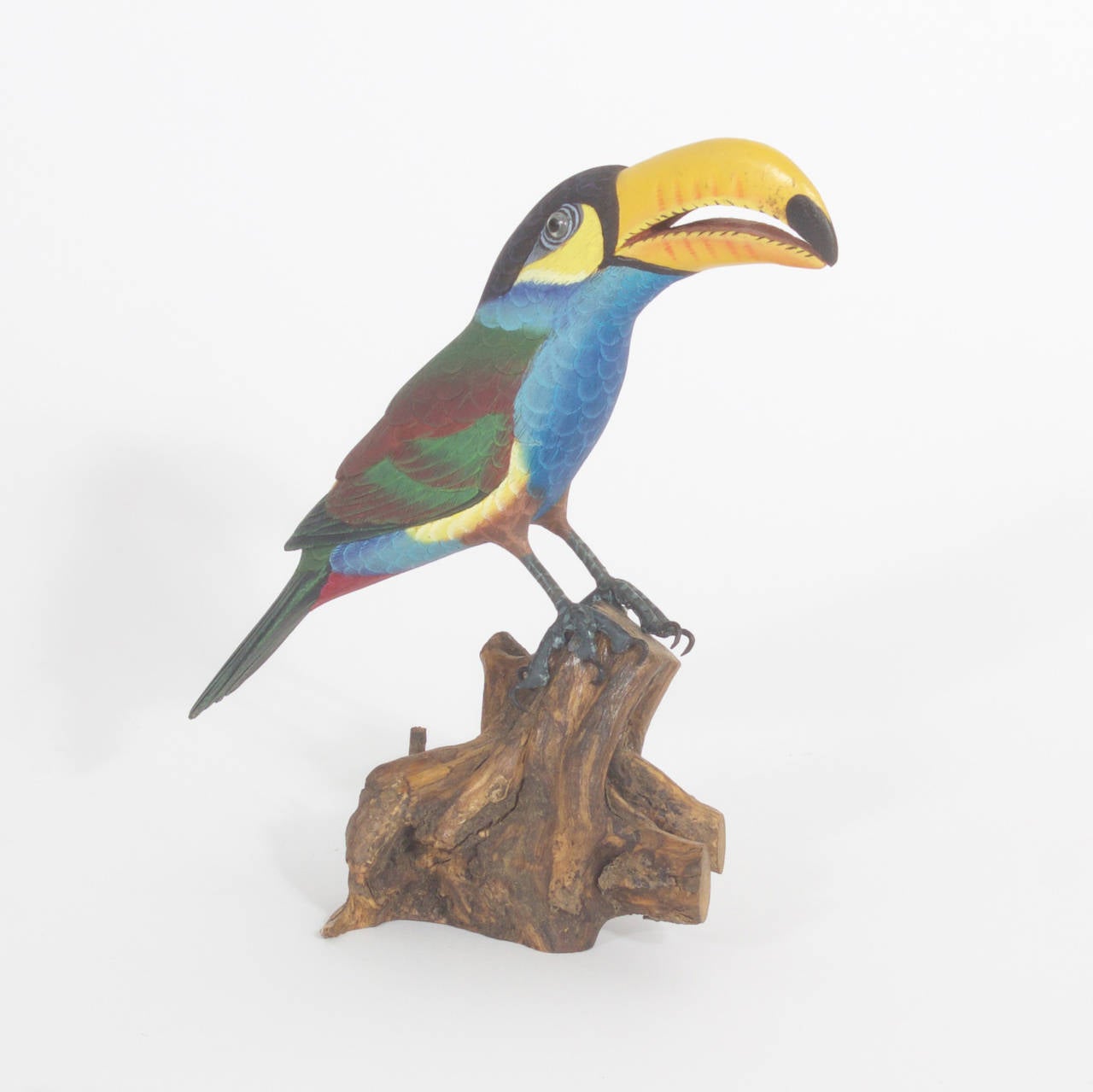 Carved and painted wood Toucan. Expertly carved and painted with unexpected life like details and brilliant colors. Featuring real bird talons attached to the feet and glass eyes and presented on a tree branch. We have 2 parrots by the same maker.