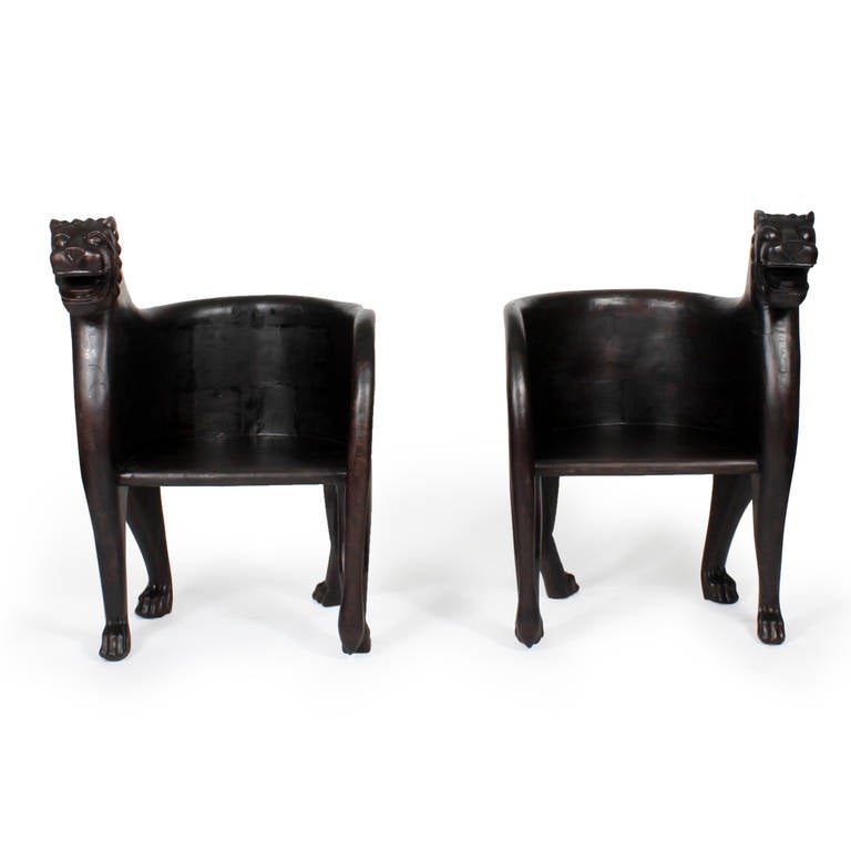An exciting pair of large scale carved hardwood arm chairs with lion heads, tails, and legs executed in the style of ancient Egyptian furnishings but with a modern twist. Flowing, graceful lines with an air of importance, perfect for channeling the