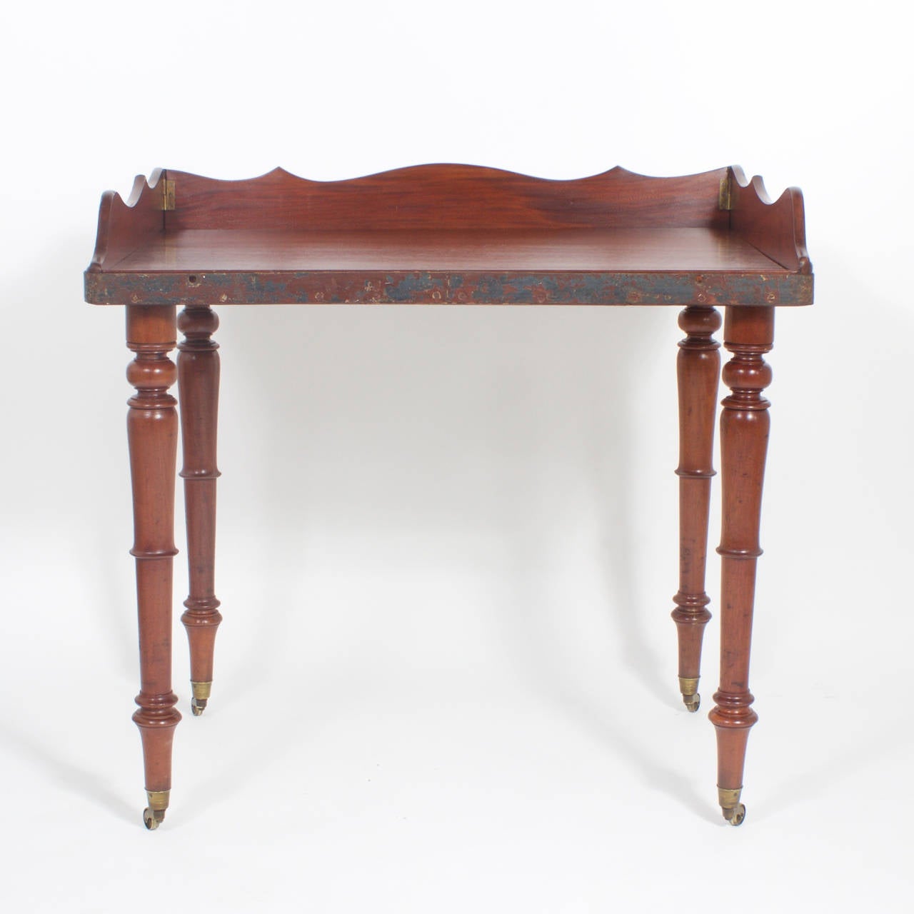 Antique Campaign mahogany table or writing desk with removable scalloped gallery and detachable turned legs. Featuring an iron band around the edge with the original worn paint and brass caster feet. This unusual piece would also serve well as a bar