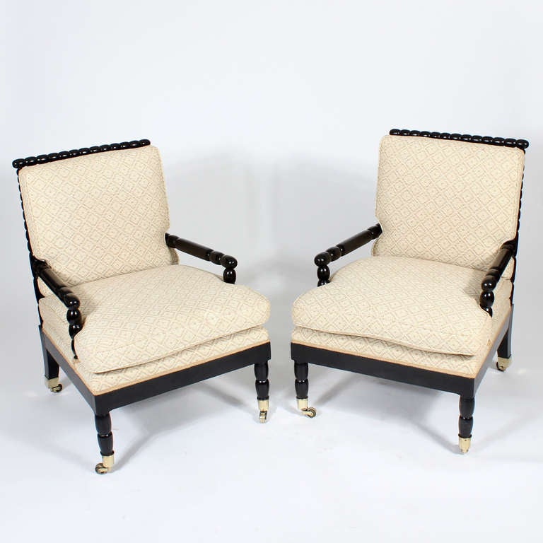 A pair of bobbin or spool turned armchairs with an ebonized finish, with spool or bobbin turned backs, legs and arms, brass cup casters and canted back legs. 

