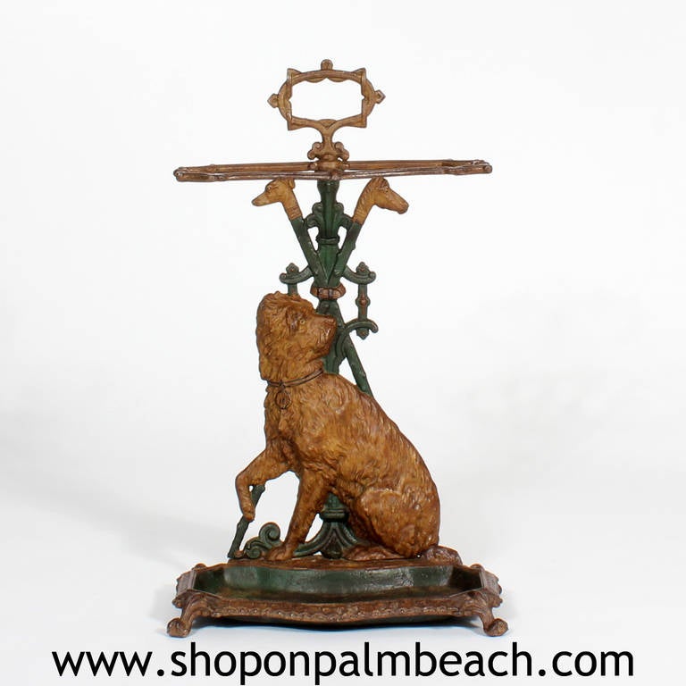 A wonderful cast iron umbrella stand, painted in green and ochre with a dog, probably a terrier, as the central figure. Horse and dog heads embellish the top of the stand. The umbrella stand is perfect for the entry way of a country estate. A really