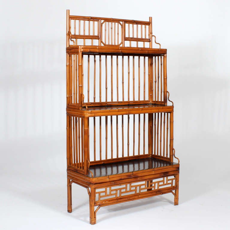 A rattan or bamboo bookcase, with black lacquered shelves, 3 tiers and with Chinese Chippendale motif blackboard and skirt.  Great color to the rattan.