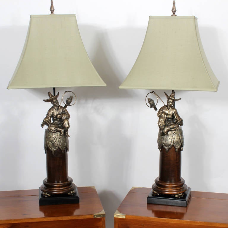 Pair of Chinoiserie style bronze and wood table lamps depicting men with parrots on a perch atop turned wood columns with frog feet on ebonized bases. Excellent quality bronze casting and whimsical composition. Newly polished and wired. Possibly