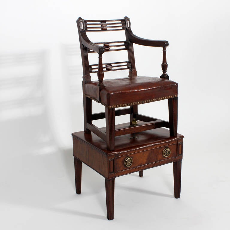 Un seggiolone per bambini in mogano di epoca georgiana su un supporto staccabile a un cassetto. La sedia ha un sedile in pelle di bue con tac in ottone, braccioli con volute in rilievo su sostegni torniti con gambe affusolate in rilievo e un