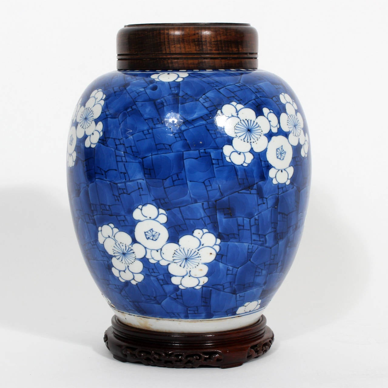 Striking, deep blue and white Chinese Export ginger jar with hardwood lid and carved base. Painted in a white cherry blossom motif. Bold and beautiful. 
Late 19th or early 20th century Old paper label on the bottom.

 