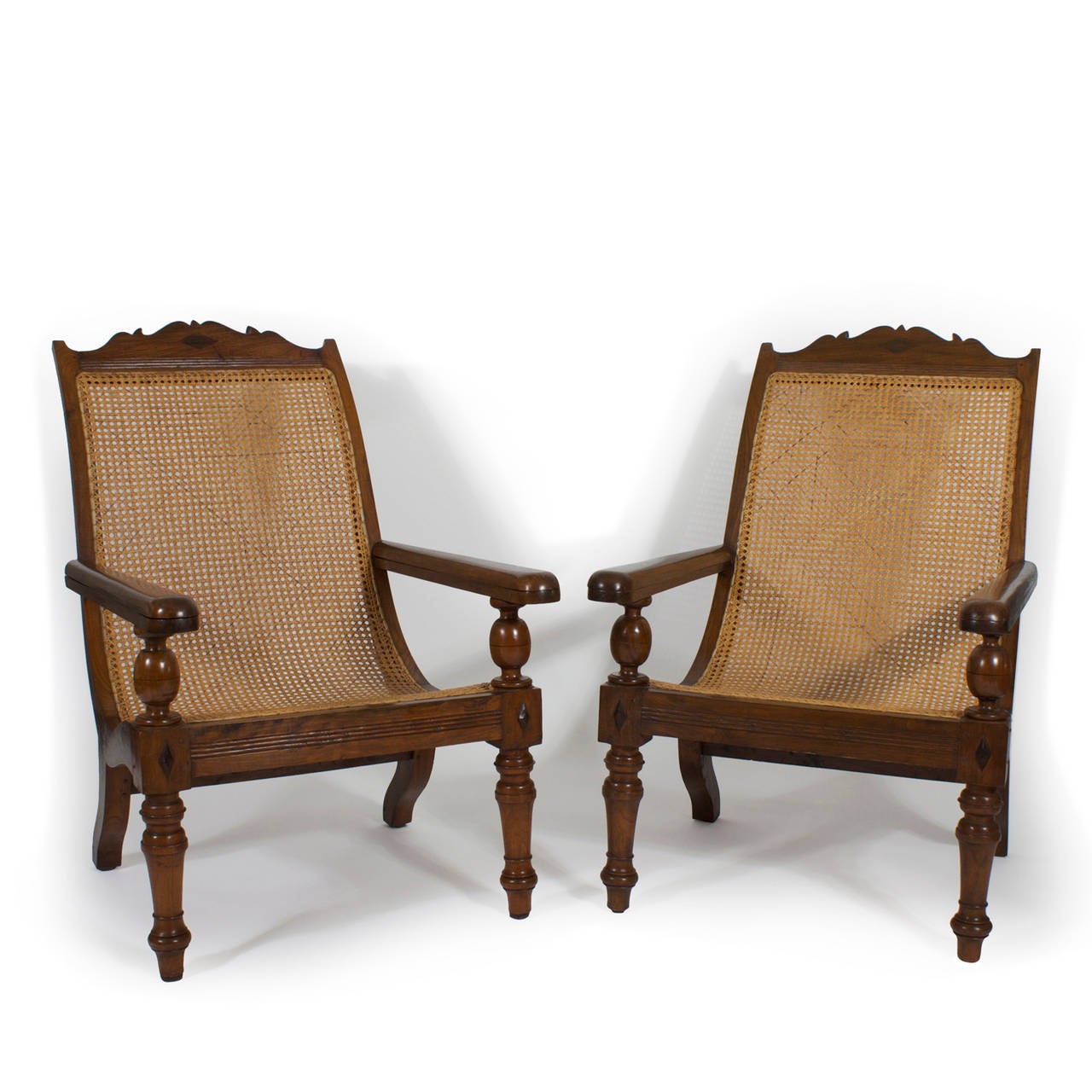 A fine pair of late 19th century or early 20th century planters chairs, in tropical hardwood with caned seats and backs, reeded and applied diamond decoration and great turnings with, of course, the prerequisite extending arms to use leg rests, for
