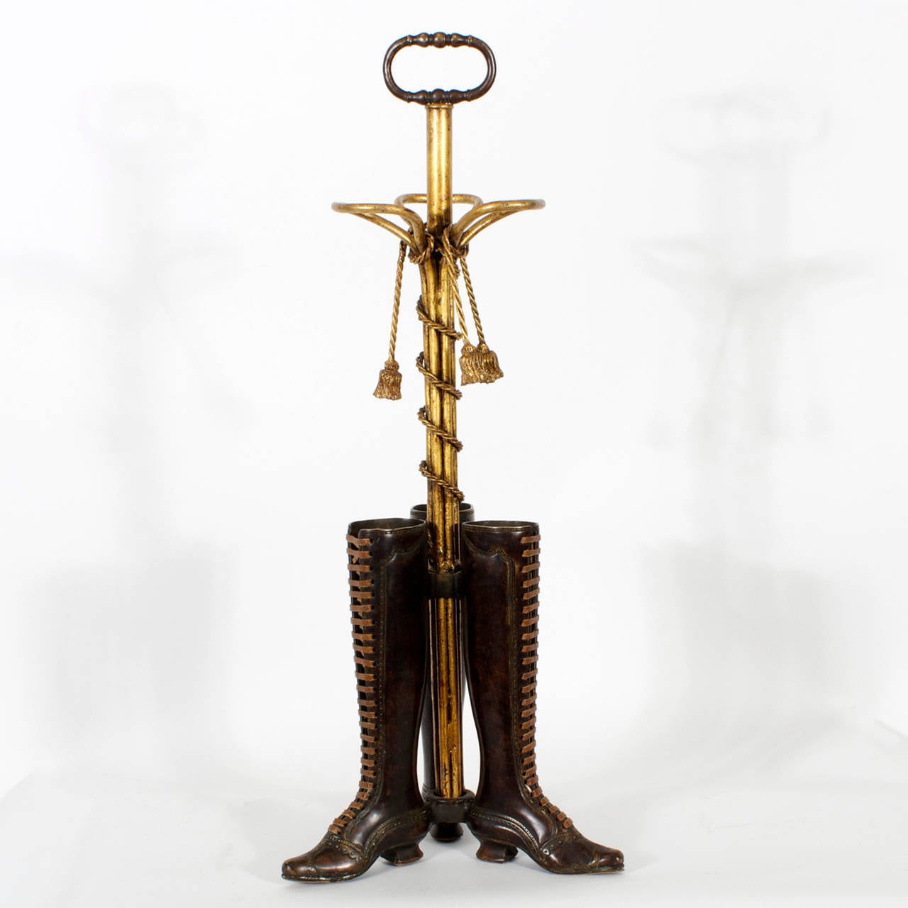 Whimsical Edwardian style umbrella stand composed of 3 bronze boots with leather laces and soles , supported by a gilded iron post, wrapped with faux rope and tassels, topped with a loop handle. Your umbrellas will thank you.