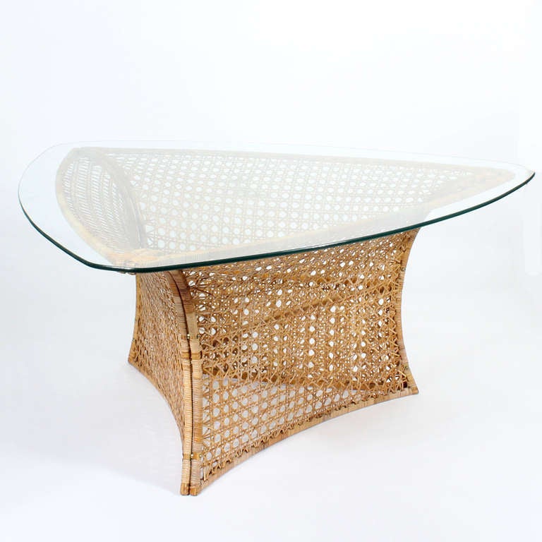 This is an amazing Mid-Century Modern  rattan dining or center table,  by Danny Ho Fong, with a triangular glass top, the base made of three concave panels of cane or wicker, that abut at the seams and join with three removable screws allowing for