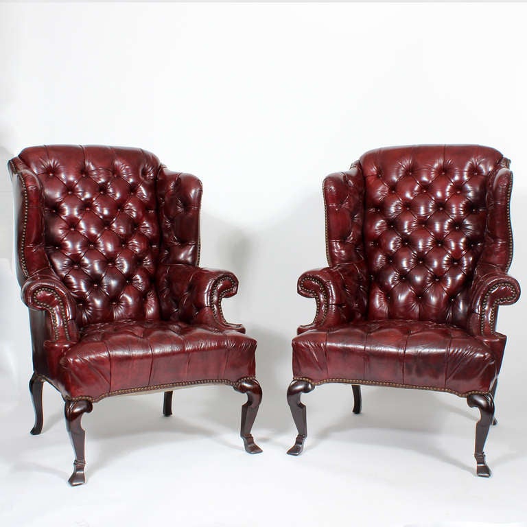 A pair of red leather tufted high back wing chairs, with great form to the brass tack accented wings, rolled arms and skirt, raised on a high, well shaped Spanish type leg.  These chairs are fantastic lookers.