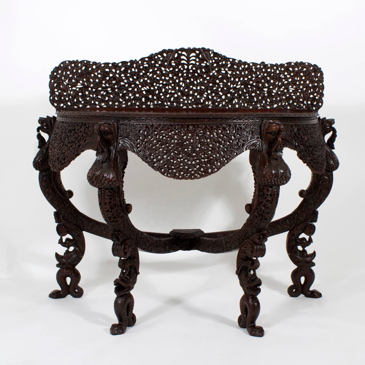 A 19th century Anglo-Indian demilune console table, in Bombay blackwood with carved legs depicting mythological serpents and bowed stretchers connecting to a center pad. Carved filigree skirts and back splash all done in an impressive bold