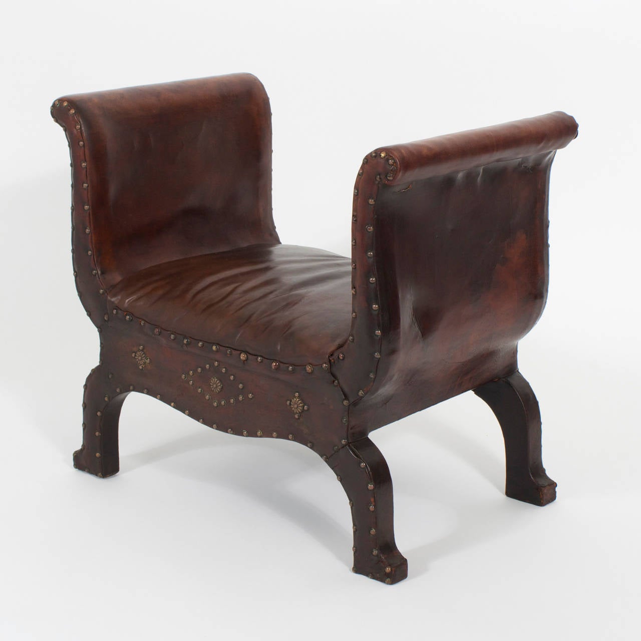 An unusual, vintage brown leather foot stool with a wood frame and saddle shape, decorated with brass studs, strong in form with a scalloped base and well formed leg. Newly polished.