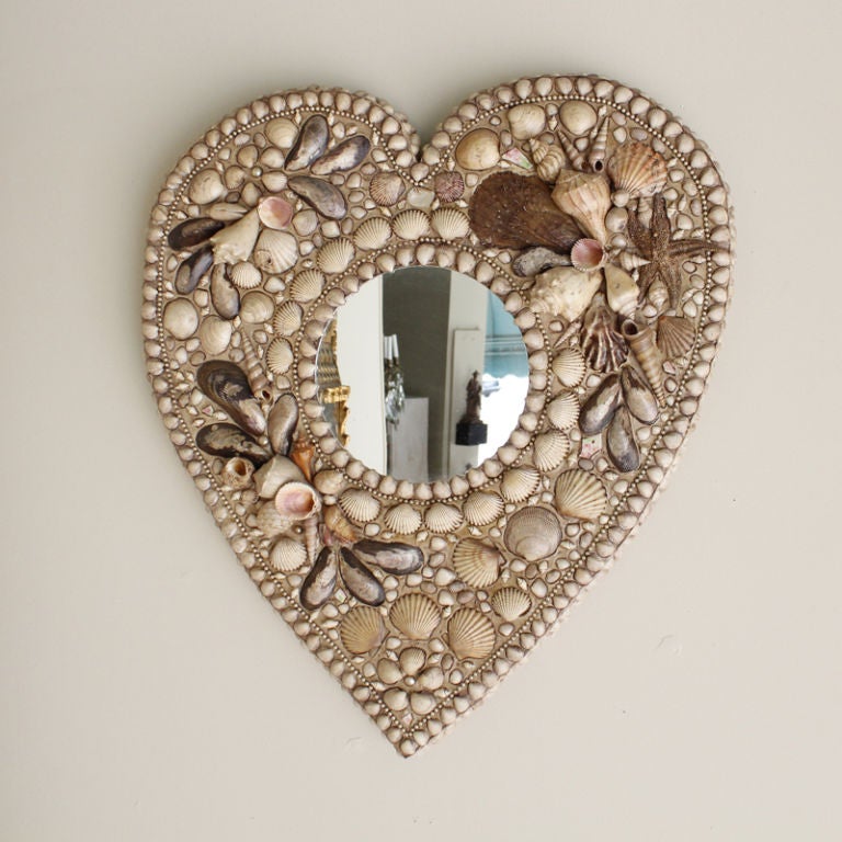 A heart shaped shell encrusted mirror frame. Favorite shell picks, line the heart shape frame and the round mirror. Made by Gael Ryan.

