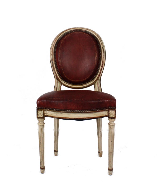 A set of white painted Louis XVI style dining chairs, with brass tacked leather seats and backs. Beautiful form and fabulously aged paint and leather.
