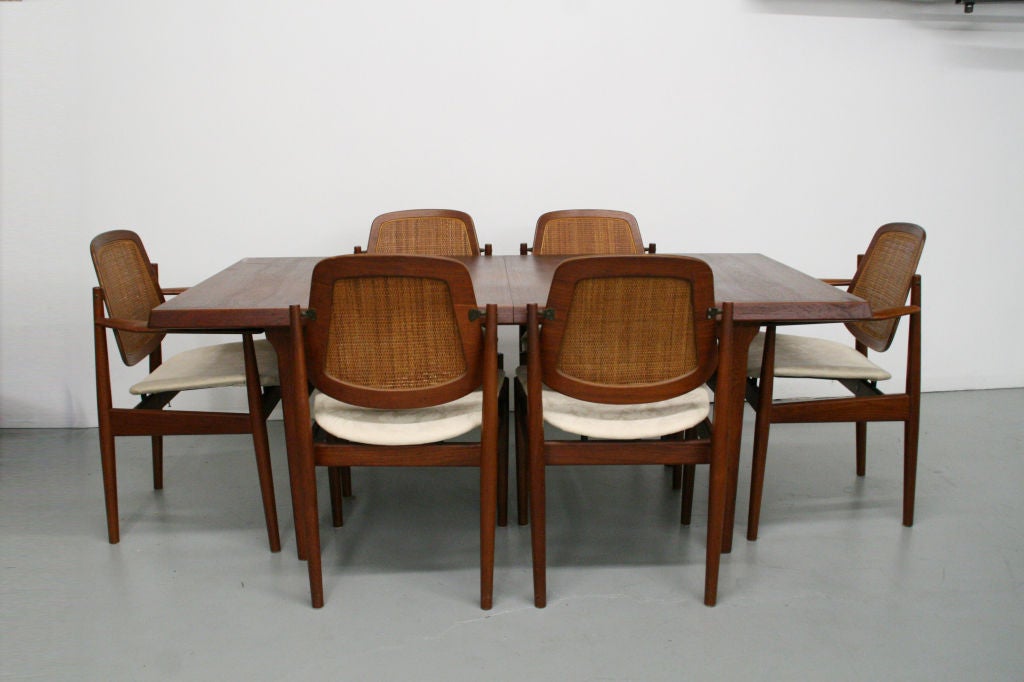 Beautiful teak dining set, designed c. 1950s. Rare and comfortable backs that rotate back and forth with your back as you move for comfort and support. Made entirely of teak with cane woven backs, with floating white fabric seats.

Table has an
