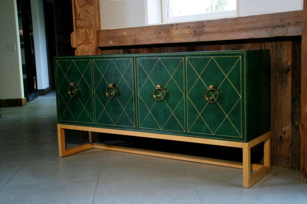 A rare Tommi Parzinger cabinet for Charak Modern c. 1950s. Completely covered in deep green leather, with gold details, amazing round brass door knocker pulls, sits and connected to a light original finish wood frame. So elegant and classic.